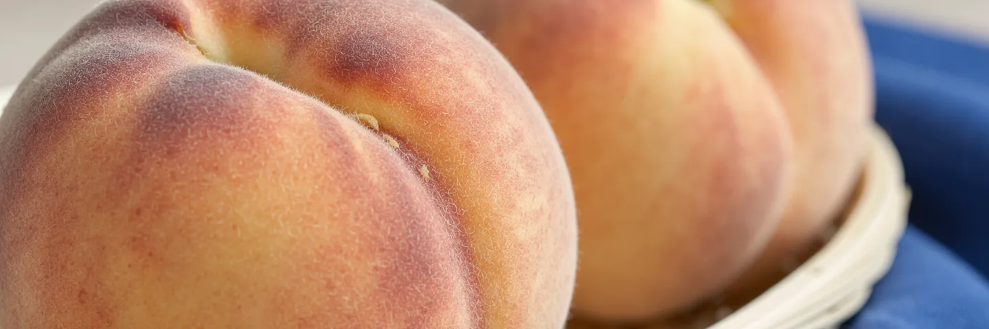 Fine peach fuzz lit from the side above a narrow edge of blue cloth and a woven basket rim